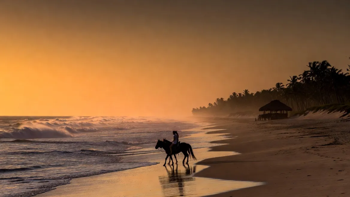 Horseback riders on the empty sweep of Playa Palmarito at sunset