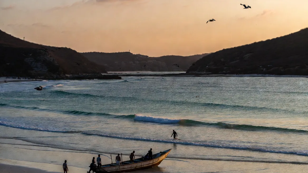 A Puerto Escondido morning taking shape: pangas loading, surfers walking out, pelicans overhead